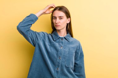 Genç, güzel bir kadın kafası karışmış ve kafası karışmış, başını kaşıyor ve yan tarafa bakıyor.