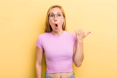 Genç, sarışın bir kadın inançsızlıktan şaşkın şaşkın bakıyor, yan taraftaki objeyi işaret ediyor ve 