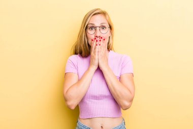 Genç sarışın kadın mutlu ve heyecanlı, şaşırmış ve şaşırmış elleri ağızda, tatlı bir ifadeyle kıkırdıyor.