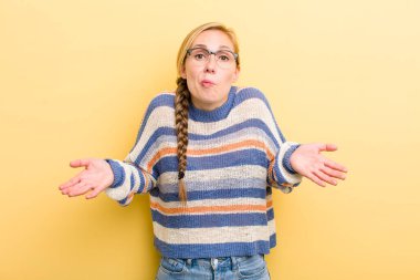 young adult  blonde woman feeling clueless and confused, having no idea, absolutely puzzled with a dumb or foolish look