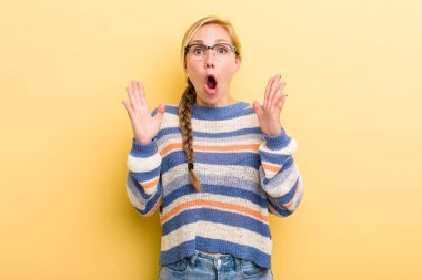 young adult  blonde woman looking shocked and astonished, with jaw dropped in surprise when realizing something unbelievable