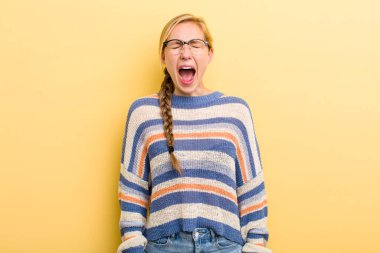young adult  blonde woman shouting aggressively, looking very angry, frustrated, outraged or annoyed, screaming no