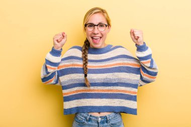 Genç sarışın kadın mutlu, şaşırmış ve gururlanmış hissediyor, bağırıyor ve başarıyı büyük bir gülümsemeyle kutluyor.