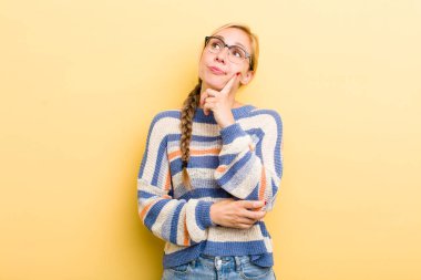 young adult  blonde woman with a concentrated look, wondering with a doubtful expression, looking up and to the side