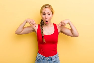 Genç sarışın kadın şok olmuş, ağzı açık ve şaşırmış hissediyor. İnançsızlığa ve şaşkınlığa doğru bakıyor ve işaret ediyor.