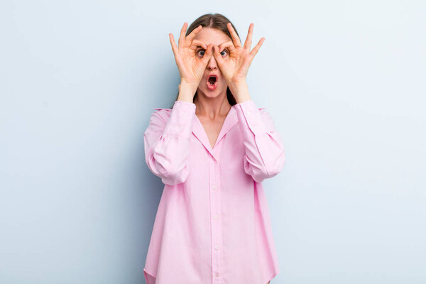 молодая взрослая красивая женщина шокирована, удивлена и удивлена, держа очки с удивленным, неверным взглядом