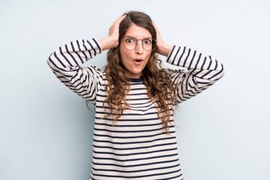 Genç ve güzel bir kadın heyecanlı ve şaşırmış görünüyor, ağzı açık, iki eli de başında, şanslı bir kazanan gibi hissediyor.