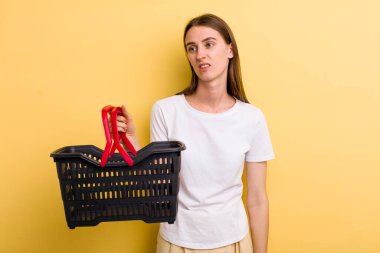 Genç ve güzel bir kadın elinde boş bir alışveriş sepeti tutuyor.