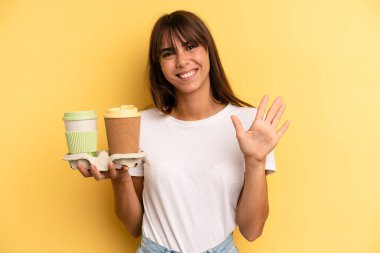 smiling and looking friendly, showing number five. take away coffees