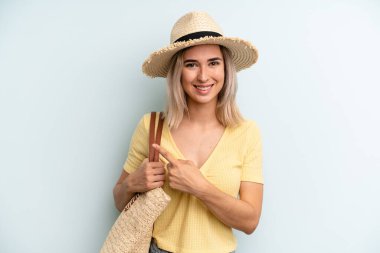blonde woman smiling cheerfully, feeling happy and pointing to the side. summer concept