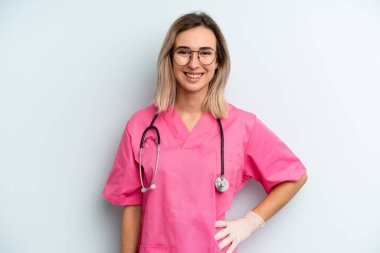 Sarışın kadın mutlu bir şekilde gülümsüyor, eli kalçasında ve kendinden emin. hemşire konsepti