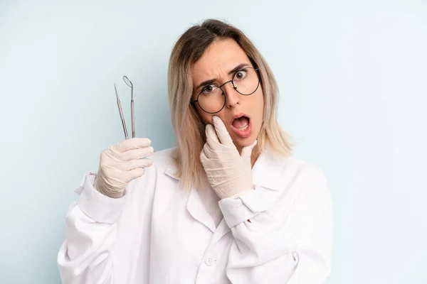 blonde woman with mouth and eyes wide open and hand on chin. dentist concept