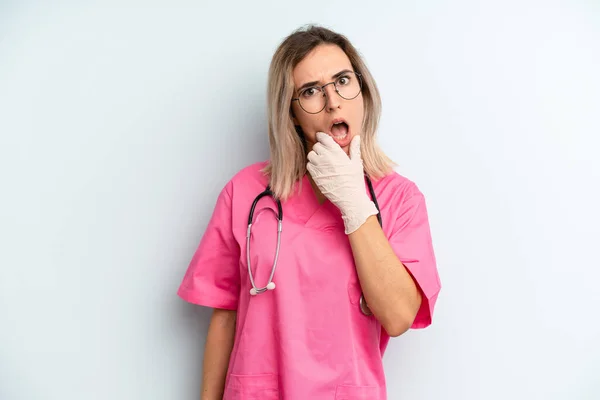 blonde woman with mouth and eyes wide open and hand on chin. nurse concept