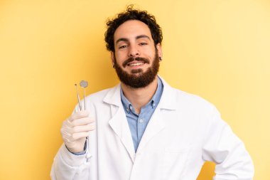 Genç adam mutlu bir şekilde gülümsüyor, eli kalçasında ve kendinden emin. dişçi kavramı