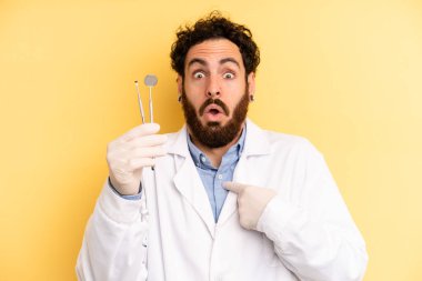 Şok olmuş ve ağzı açık, kendini işaret eden genç bir adam. dişçi kavramı