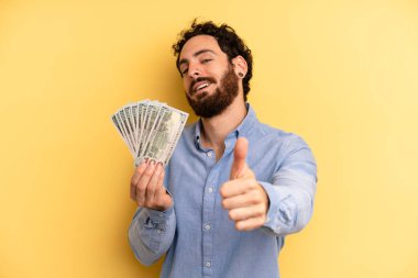Genç adam gururlu, olumlu bir şekilde gülümsüyor. Dolar banknotları konsepti