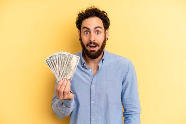 Genç adam çok şaşırmış ya da şaşkın görünüyor. Dolar banknotları konsepti
