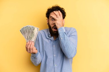 Delikanlı şok olmuş, korkmuş ya da korkmuş görünüyor, yüzünü eliyle kapatıyor. Dolar banknotları konsepti