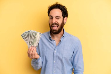 Neşeli ve asi tavırlı genç bir adam, şaka yapıyor ve dilini dışarı çıkarıyor. Dolar banknotları konsepti