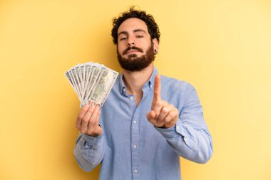 Genç adam gülümsüyor ve arkadaş canlısı görünüyor, bir numarayı gösteriyor. Dolar banknotları konsepti