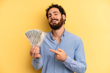 Genç adam neşeyle gülümsüyor, mutlu hissediyor ve bir tarafı işaret ediyor. Dolar banknotları konsepti