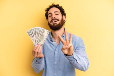 Genç adam gülümsüyor ve arkadaş canlısı görünüyor, üç numarayı gösteriyor. Dolar banknotları konsepti