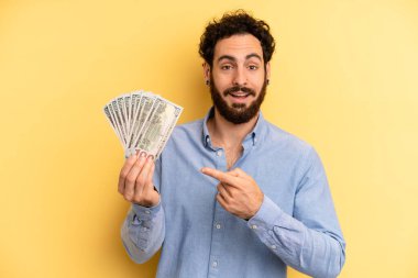 Genç adam heyecanlı ve şaşırmış görünüyor. Dolar banknotları konsepti
