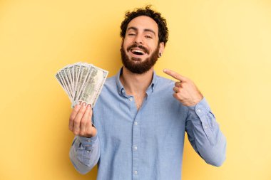 Genç adam kendine güvenerek kendi gülüşünü işaret ediyor. Dolar banknotları konsepti