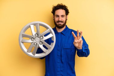 Genç adam gülümsüyor ve arkadaş canlısı görünüyor, üç numarayı gösteriyor. araba mekaniği kavramı