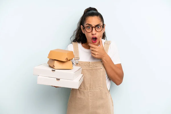 hispanic woman with mouth and eyes wide open and hand on chin. fast food take away concept