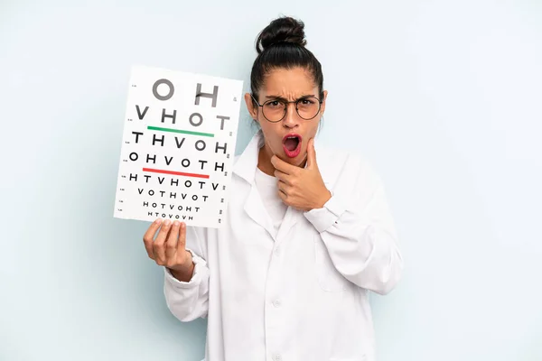 hispanic woman with mouth and eyes wide open and hand on chin. optical vision test concept
