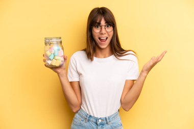 hispanic woman feeling happy and astonished at something unbelievable. candies bottle concept