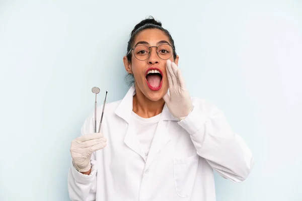 hispanic woman feeling happy,giving a big shout out with hands next to mouth. dentist concept