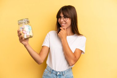 hispanic woman smiling with a happy, confident expression with hand on chin. candies bottle concept