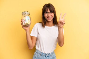 hispanic woman smiling and looking happy, gesturing victory or peace. candies bottle concept