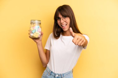 hispanic woman feeling proud,smiling positively with thumbs up. candies bottle concept