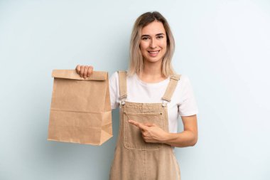 Sarışın kadın neşeyle gülümsüyor, mutlu hissediyor ve bir tarafı işaret ediyor. teslimat kavramını kaldır