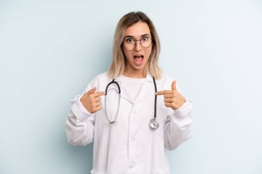 Sarışın kadın kendini mutlu hissediyor ve heyecanlı bir şekilde kendini işaret ediyor. tıp öğrencisi konsepti