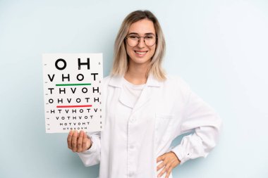 Sarışın kadın mutlu bir şekilde gülümsüyor, eli kalçasında ve kendinden emin. optik görüş testi konsepti