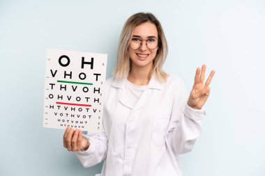 Sarışın kadın gülümsüyor ve arkadaş canlısı görünüyor, üç numarayı gösteriyor. optik görüş testi konsepti