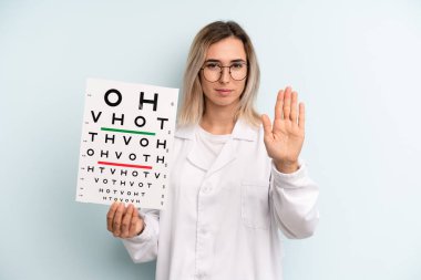 Sarışın kadın ciddi görünüyor. Avuç içi gösteriyor. Durma hareketi yapıyor. optik görüş testi konsepti