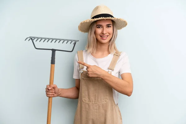 Blonde Woman Smiling Cheerfully Feeling Happy Pointing Side Farmer Rake — Fotografia de Stock