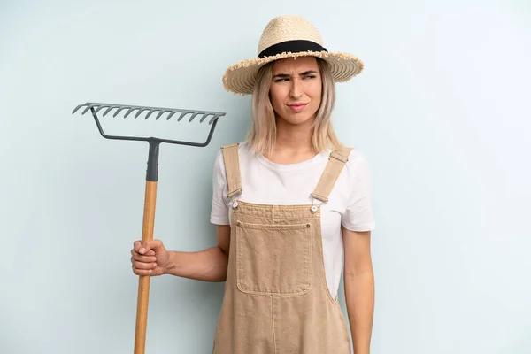 blonde woman feeling sad, upset or angry and looking to the side. farmer and rake cocnept