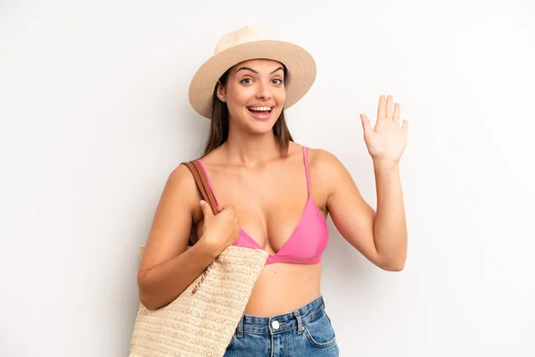 pretty girl smiling happily, waving hand, welcoming and greeting you. summer and hat concept