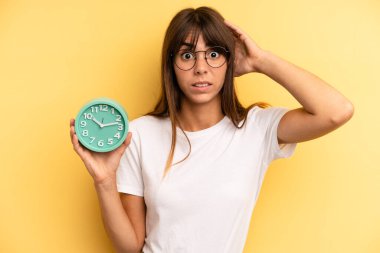 hispanic woman feeling stressed, anxious or scared, with hands on head. alarm clock concept