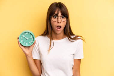 hispanic woman looking very shocked or surprised. alarm clock concept