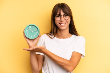 hispanic woman smiling cheerfully, feeling happy and showing a concept. alarm clock concept
