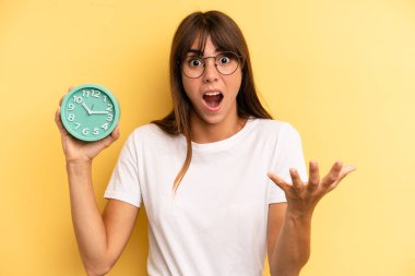 hispanic woman amazed, shocked and astonished with an unbelievable surprise. alarm clock concept
