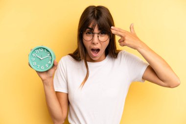 hispanic woman looking unhappy and stressed, suicide gesture making gun sign. alarm clock concept