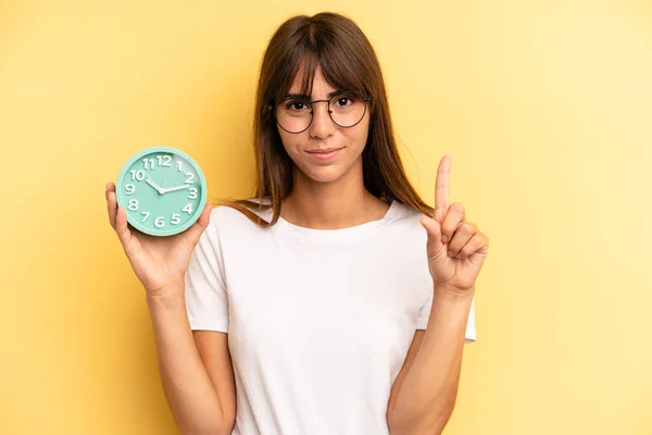 Hispanic Woman Smiling Looking Friendly Showing Number One Alarm Clock — ストック写真